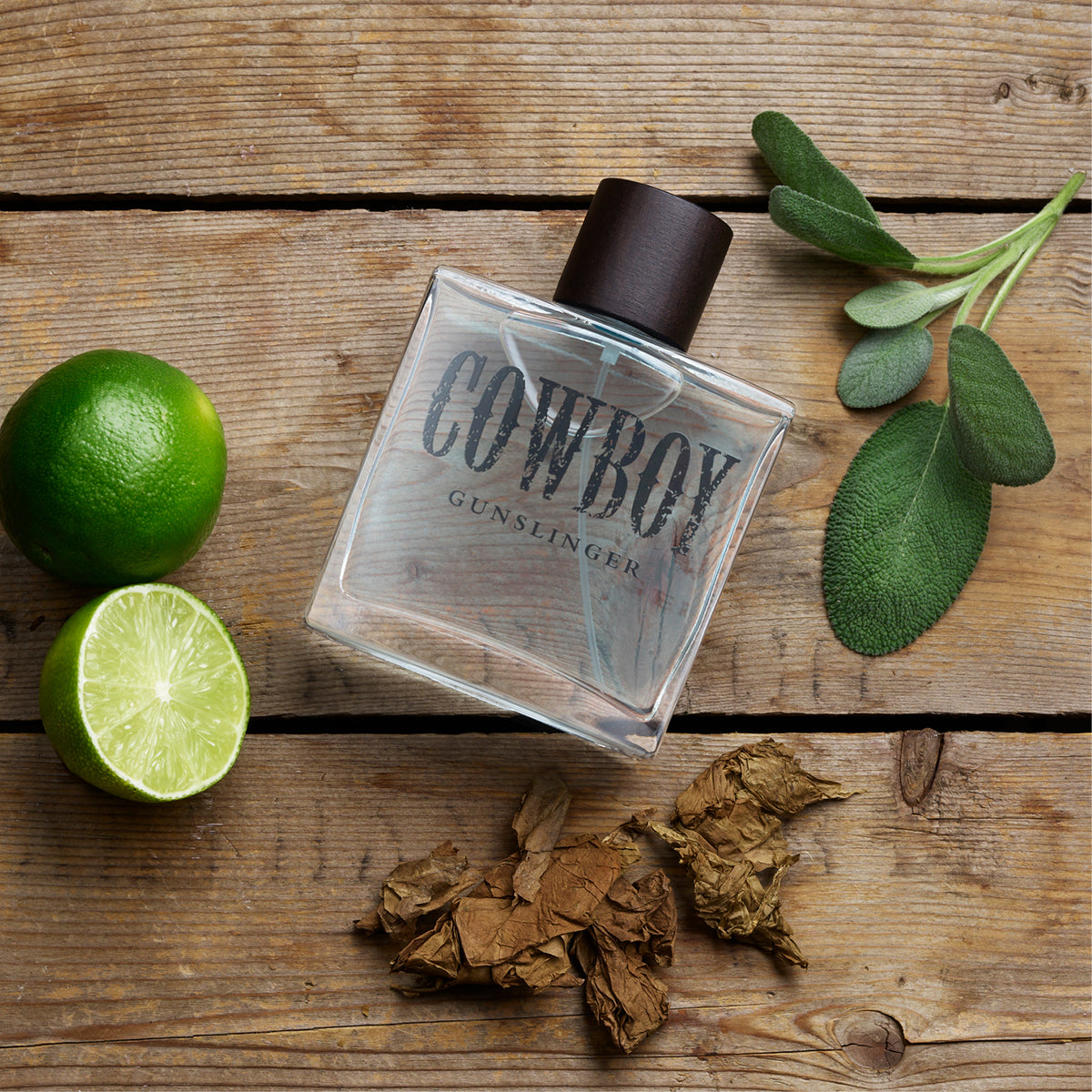 Cowboy Gunslinger cologne bottle on wood with limes and tobacco leaves